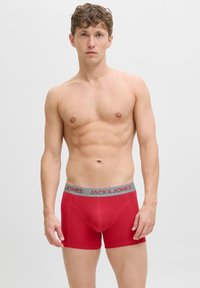 Oben ohne Mann in roten Boxershorts mit grauem Bund, auf dem "JACK & JONES" steht, steht vor einem schlichten weißen Hintergrund.