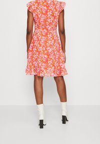 Blumenkleid mit kurzen, gerafften Ärmeln, lebendiger orange Hintergrund, pinke und lila Blumen, knielang mit ausgestellt Saum. Weiße Knöchelstiefel.