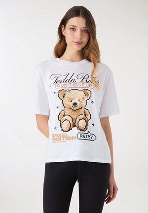 Maglietta bianca in cotone con grafica di un orsetto pixelato, scritte nere e un'etichetta arancione con la scritta "PIXEL EDITION" e "RETRY."