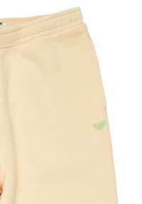 Licht perzik kleurige joggingbroek van zachte stof, met een rekbare tailleband en een klein groen geborduurd logo aan de onderzijde aan de linkerkant.