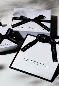 Cajas de regalo blancas con cintas negras, que presentan el nombre de la marca "LATELITA" en tipografía moderna y en negrita. Tamaños variados, diseño limpio.
