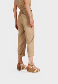 Giocattolo in tessuto leggero color beige con vita arricciata e caviglie a polsino, abbinato a sandali con zeppa bicolore con cinturini regolabili.