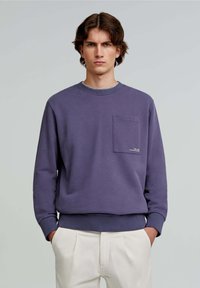 Paarse katoenen sweatshirt met lange mouwen, ronde hals en een voorkantzak met een geborduurd logo. Gecombineerd met beige broeken.