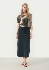 Gestreepte beige en zwarte top met korte mouwen, gecombineerd met een lange donkergroene rok met een trekkoord in de taille, en zwarte sandaaltjes met bandjes.