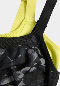 Sport-bh med ett svart camouflage-mönster ovanpå och en starkt gul mesh-bak. Har justerbara axelband och en slät yta för komfort.