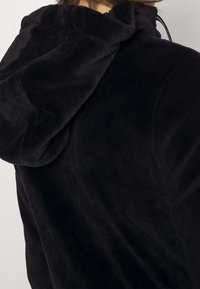 Black, hooded sweatshirt made of soft fleece material. Features a textured surface and adjustable drawstrings on the hood for fit.