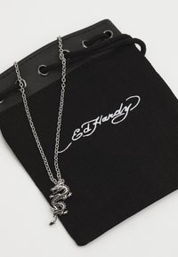 Colar de pingente de dragão prateado em um saco de tecido preto com o logótipo branco "Ed Hardy", apresentando uma corrente resistente e detalhes em ilhós.