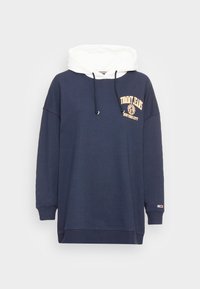 Námornícky modrá nadmerná mikina s bielou kapucňou, s zlatým logom a grafickým zobrazením leva na hrudi. Vyrobená z mäkkej látky s rebrovanými manžetami.