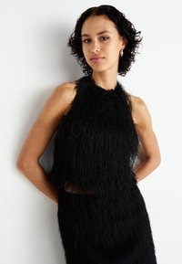 Black cropped halter top made from fringed fabric. Features a high neckline and a textured finish, paired with a matching skirt.