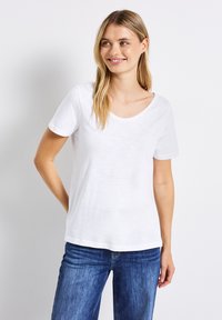 Hvid bomulds T-shirt med korte ærmer, rund halsudskæring, afslappet pasform og en glat tekstur. Båret med blå denim jeans.