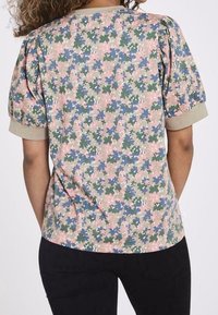 Top de manga corta con un patrón floral en rosa, verde y azul sobre un fondo beige; presenta mangas abullonadas y un cuello redondo.