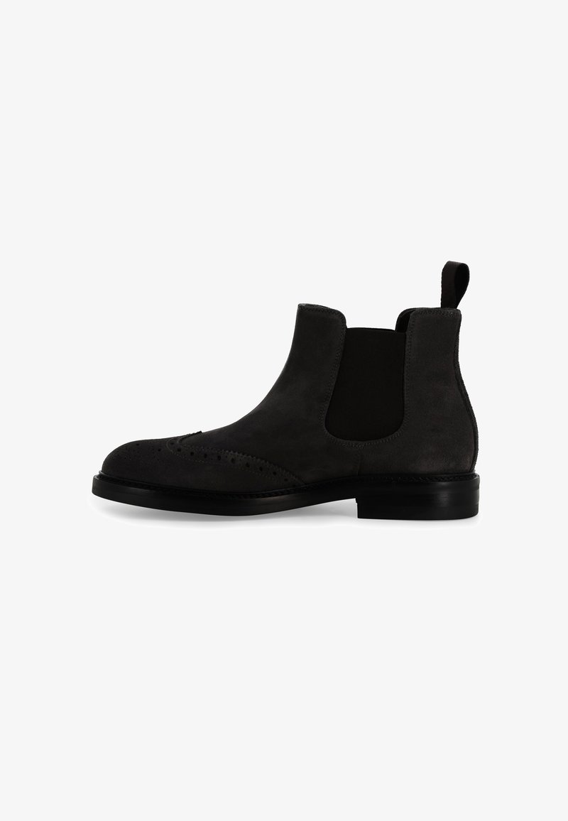 Stivaletto Chelsea in camoscio nero con pannelli laterali elastici, punta rotonda, dettagli brogue sulla punta e suola in gomma nera bassa.