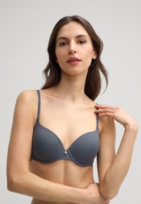 Gray padded bra featuring adjustable straps, a central decorative accent, and lace detailing along the band with a smooth, matte finish.