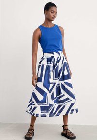 Sinisen tank topin yhdistelmä valkoisen hameen kanssa, jossa on rohkeita sinisiä geometrisia kuvioita. Hameessa on korkea vyötärö ja virtaava muoto.