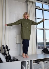 Alyvuogių žalios spalvos vandeniui atspari striukė su aukštu kaklu, ilgomis rankovėmis ir reguliuojamais raišteliais. Turi priekines kišenes ir laisvą siluetą.