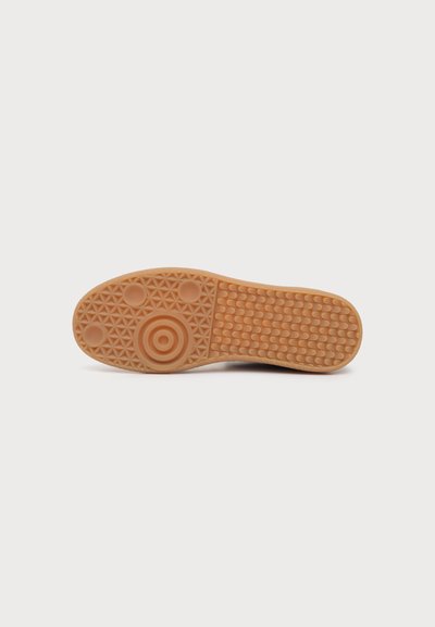 Semelle de chaussure avec une bande de roulement en caoutchouc texturée comprenant des motifs circulaires et des grilles pour l'adhérence, montrée sur un fond blanc uni.