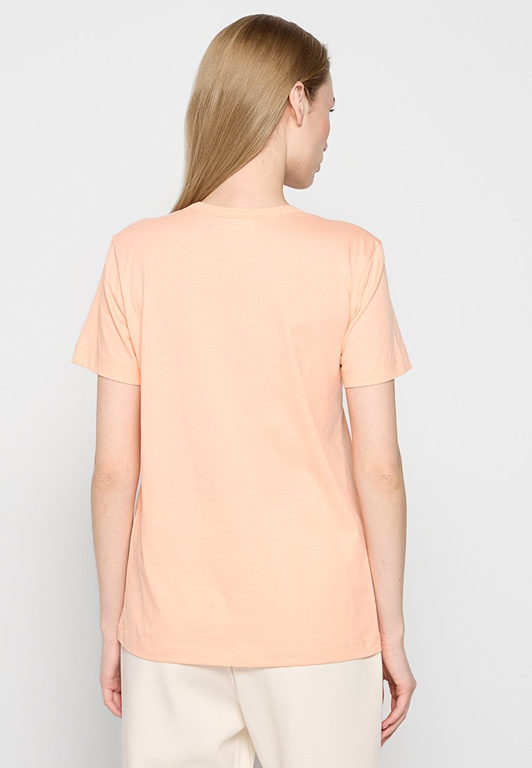 T-shirt di cotone color pesca, maniche corte, scollatura rotonda, morbido al tatto, vestibilità rilassata, branding minimale, design della schiena semplice.