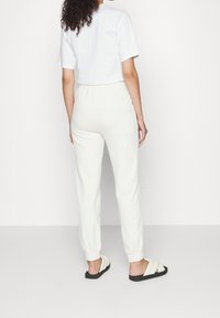 Bílá košile s krátkým rukávem, smetanové jogger kalhoty s elastickými manžetami a černé skluzové sandály. Tento outfit má uvolněný střih a jednoduchý design.