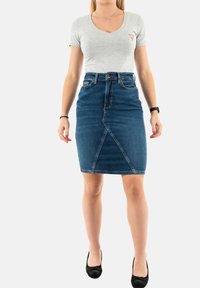 T-shirt gris clair à col en V associé à une jupe crayon en denim taille haute. La jupe présente un détail de couture à l'avant et un lavage bleu foncé.