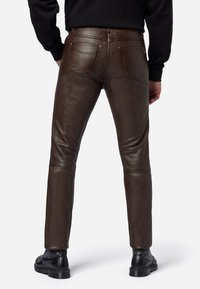 Bruine leren broek met een slim fit, voorzien van twee achterzakken en een subtiele glans. De silhouet is op maat gemaakt met strakke lijnen en stiksels.