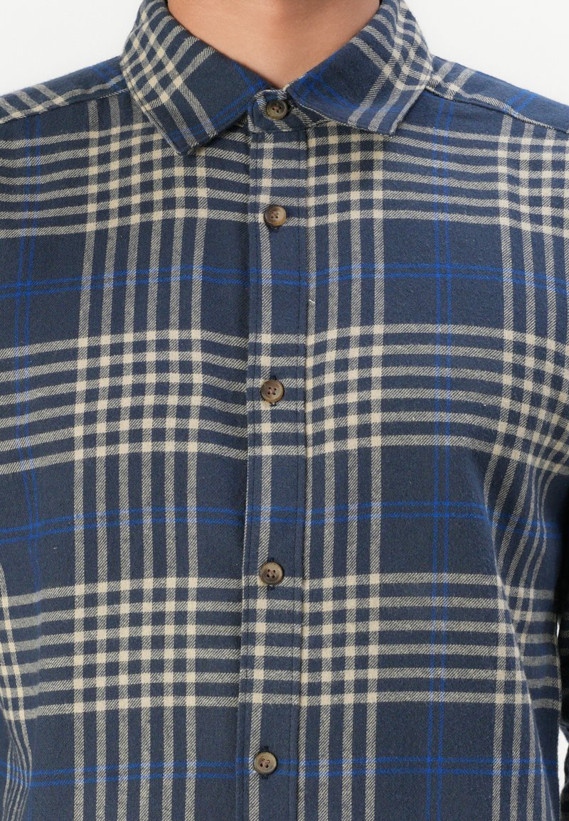 Karierte Button-up-Hemd in Marineblau und Creme mit blauen Akzenten. Hergestellt aus einem strukturierten Stoff mit einem feststehenden Kragen und braunen Knöpfen.