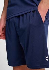 Granatowe szorty sportowe wykonane z miękkiego, elastycznego materiału, z elastycznym paskiem w talii, bocznymi kieszeniami oraz białym detalem w kształcie trójkąta z logo.