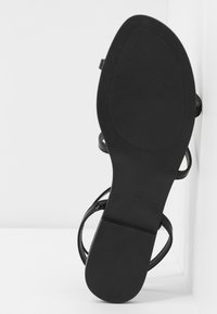 Sandale noire avec une semelle lisse et une prise texturée. Comprend des lanières fines pour un design ouvert, mettant en valeur une esthétique minimaliste.