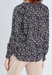 Chemise en tissu noir avec motif floral blanc, manches longues et coupe décontractée. Dotée d'un ourlet arrondi et de poignets boutonnés.