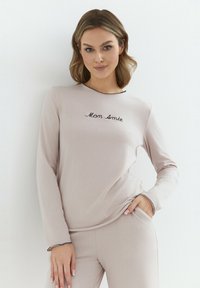 Jasnoróżowa bluzka z długimi rękawami z czarnym haftowanym napisem "Mon Amie". Miękka tkanina z okrągłym dekoltem i kontrastowym wykończeniem.