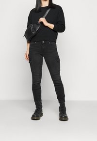 Pantalones cargo negros con múltiples bolsillos, ajuste ceñido y puños acanalados. Combinados con una sudadera negra y botas negras de cordones.