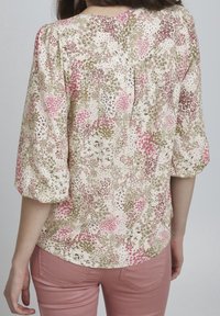 Blumenbluse aus leichtem Stoff; mit pinken, grünen und beigen Mustern; runder Ausschnitt; dreiviertel Ärmel; geraffte Details am Rücken.
