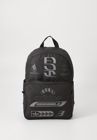 Sac à dos noir en tissu durable, présentant de grands graphismes blancs, de nombreux compartiments et une poignée supérieure pour le transport.