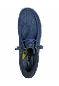 Zapato slip-on de denim marino con superficie texturizada, suela de goma, cordones elásticos y cuello acolchado. Presenta un acento amarillo en el interior.