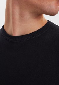 Sort ribbet bomuldscrewneck skjorte med en glat tekstur og syet halsudskæring. Nærbillede af kraveområdet.