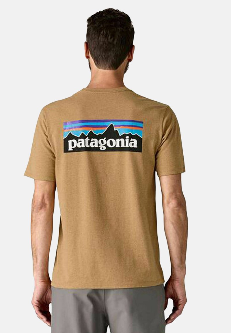 Camiseta de algodón marrón con un gráfico colorido de montañas y el texto "patagonia" en la parte posterior, de manga corta y cuello redondo.