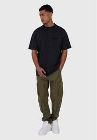 Schwarzes Baumwoll-T-Shirt mit einem schwachen Logo, kombiniert mit olivgrünen Cargo-Hosen mit mehreren Taschen und weißen High-Top-Sneakern.