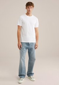 Camiseta de algodón blanca con mangas cortas, escote redondo, combinada con jeans de mezclilla azul claro y zapatillas verde menta. Diseño minimalista.