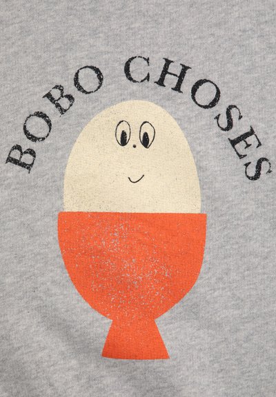 Camisa de algodón gris con un diseño impreso de un huevo sonriente en una taza naranja. El texto en la parte superior dice "BOBO CHOSES" en una fuente negra desgastada.