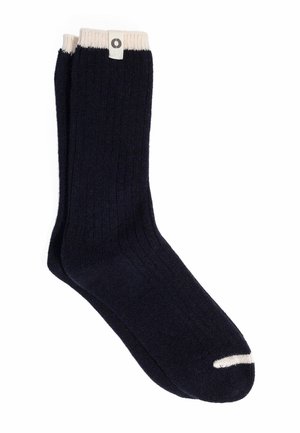 Paire de chaussettes noires côtelées avec des bords blancs et un petit détail blanc sur les orteils, posées à plat sur un fond blanc.
