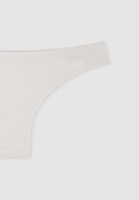 String in cotone bianco con una texture liscia, design a vita bassa e lati sottili, dotato di una fascia elastica senza cuciture per il massimo comfort.