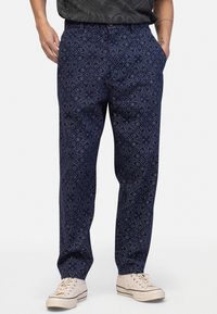 Navy patterned trousers with floral designs, relaxed fit, soft fabric, and side pockets, paired with light-colored sneakers.