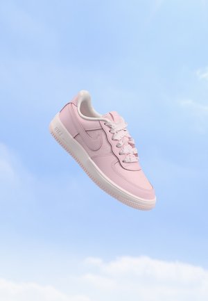 Une seule basket Nike rose clair avec des lacets blancs flottant devant un ciel bleu clair avec des nuages doux.