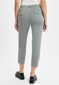 Hellgraue, taillierte Hose aus weichem Stoff mit zwei Gesäßtaschen und dezenten Stichdetails. Getragen mit schwarzen Schuhen.