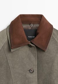 Cappotto in suede verde con colletto in suede marrone scuro e etichetta interna nera con la scritta "Massimo Dutti," abbottonato in cima e a metà.