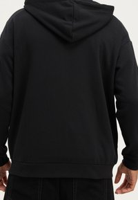 Svart sweatshirt med huva, tillverkad av mjukt material, med normal passform och ribbade muddar och nederdel, med minimal detaljering på baksidan.