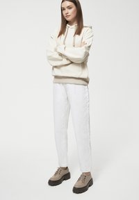 Przytłaczająca kremowa bluza z kapturem, z regulowanym sznurkiem, w połączeniu z białymi prostymi dżinsami oraz beżowymi, masywnymi butami na sznurowadła. Prosty design, luźny krój.