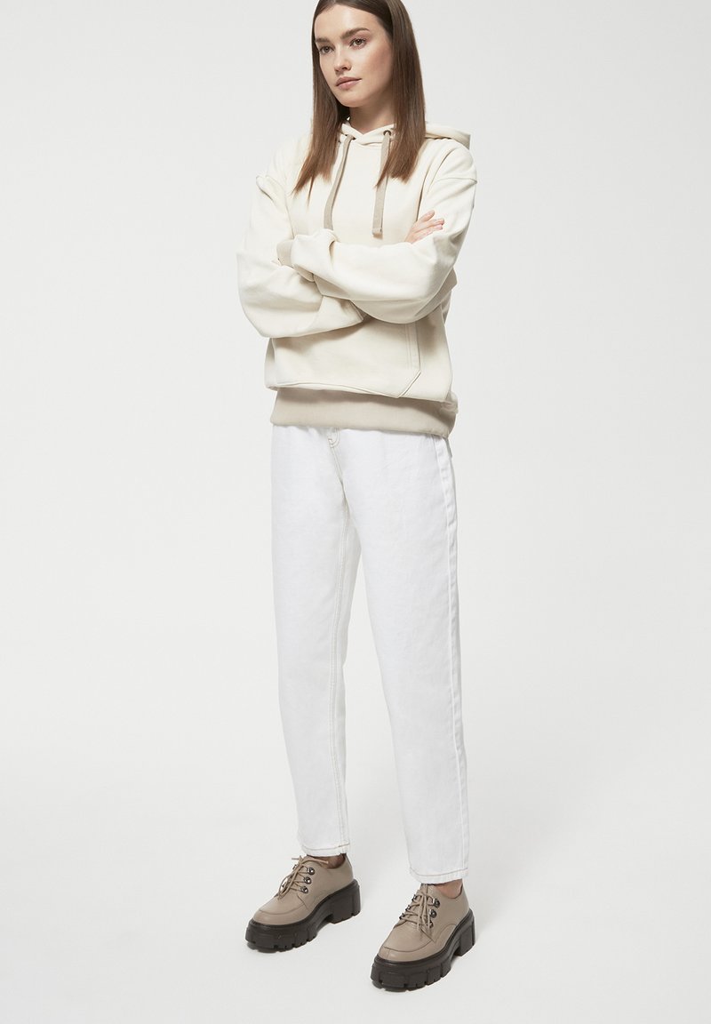 Przytłaczająca kremowa bluza z kapturem, z regulowanym sznurkiem, w połączeniu z białymi prostymi dżinsami oraz beżowymi, masywnymi butami na sznurowadła. Prosty design, luźny krój.
