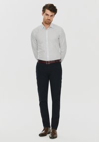 Biała koszula w czarne kropki, z zapięciem na guziki; połączona z granatowymi spodniami i brązowymi skórzanymi butami. Gładki materiał, dopasowany krój.