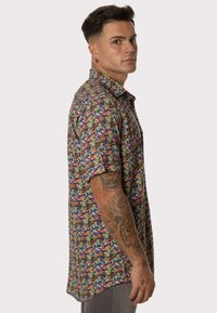 Camisa de manga corta colorida con un diseño de múltiples patrones en tonos brillantes de púrpura, verde, azul y amarillo, con un ajuste relajado.