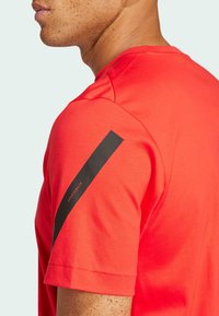 Camiseta deportiva roja con una franja diagonal negra y el texto "SPORTSWEAR" en la manga. Fabricada con material suave y transpirable.
